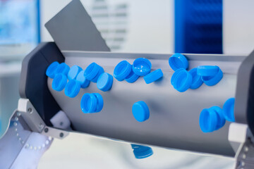 Production line - many blue plastic bottle caps falling from conveyor belt at factory, exhibition. Manufacturing, recycling, industry, technology equipment concept
