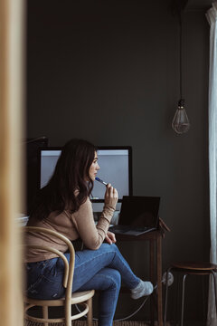 Fundersam kvinna sitter vid skrivbord hemma och tittar bort
