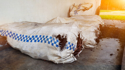 Black charcoals are stored in the white sacks which are sealed with red ropes and stored on the concrete floor closed to the white wall, edited with lens flare shining from above