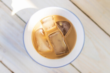 Glass of ice coffee isolated on wooden table with sunlight; top view.