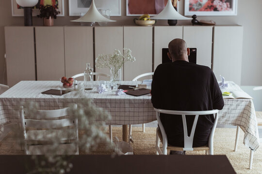 Man sitter vid matbord hemma och arbetar p&aring; laptop