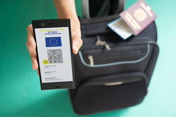Woman showing on smartphone EU Digital Covid Certificate with quad code. With passport, boarding...