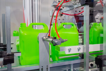 Empty green plastic jerrycans moving on conveyor belt of automatic pet blow molding machine at...