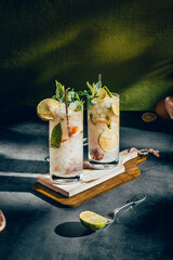Dark photography of a cold drink, a glass of mojito with mint leaf, ice, lemon and sugar on a wooden table with a vintage style.