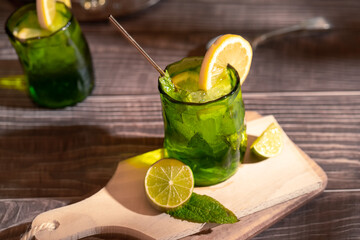 Moody dark photography of a cold drink, a glass of mojito with mint leaf, ice, lemon and sugar on a wooden table with a vintage style.