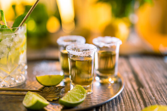 Dark photography of tequila shots with salt and lemon slices on a wooden board with copyspace.
