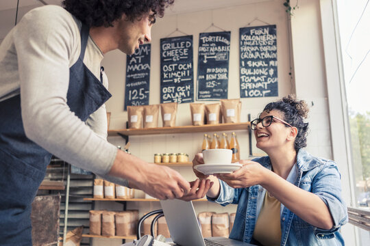 Man serverar kaffe till leende g&auml;st p&aring; caf&eacute;