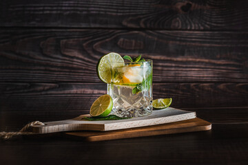 Moody dark photography of a cold drink, a glass of mojito with mint leaf, ice, lemon and sugar on a...