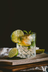 Moody dark photography of a cold drink, a glass of mojito with mint leaf, ice, lemon and sugar on a...