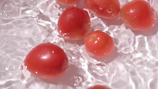 Small tomatoes falling into a container with water for cleaning. Slow motion