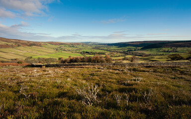 View along valley with heather moorland, fields, and trees under bright autumn sky.