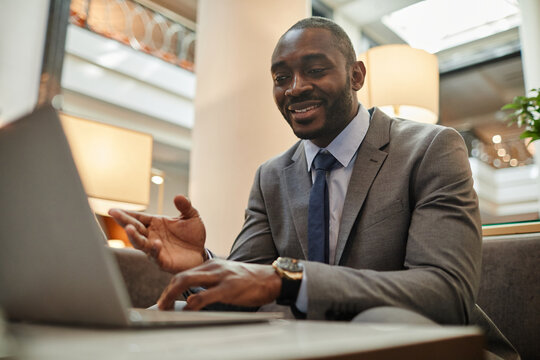Portrait of successful African-American businessman using laptop during online meeting in hotel lobby, copy space