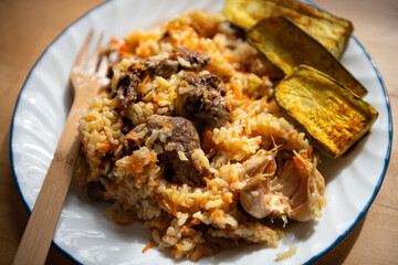 Cooked lamb meat shoulder chops, onions and carrots on plate as traditional Kazakh or Uzbek pilaf or plov macro closeup with zucchini on side