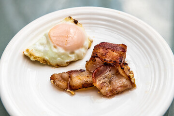 Macro closeup of cooked greasy bacon strips slices and fried egg on white plate at breakfast brunch traditional American meal