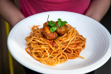 Closeup of woman hands holding red tomato sauce Italian pasta noodles and cilantro on white plate as Italian dish macro closeup with texture on meat