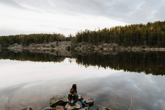 Kvinnlig utforskare sitter p&aring; sten vid sj&ouml; och tittar bort