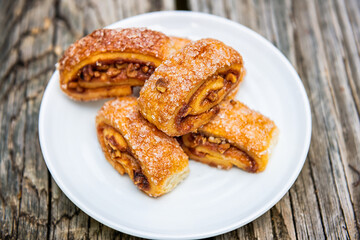 Closeup of jam nut rugelach pastry Jewish dessert on white plate and wooden table with sugar crystals texture on rolls