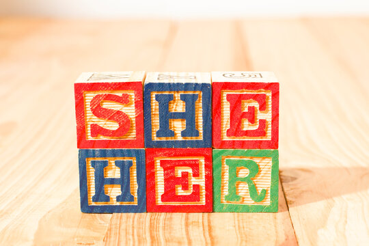 Spectacular wooden cubes with the word SHE HER on a wooden surface.