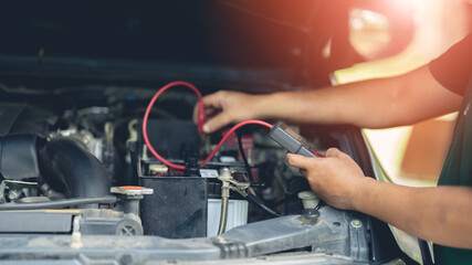 A mechanic is using a voltmeter to measure the current at the car battery.