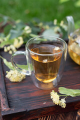 Glass cup with linden tea on dark wooden tray outdoors in summer.