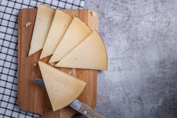 Top view of triangle pieces of cured Manchego cheese and a sharp knife on a wooden food board