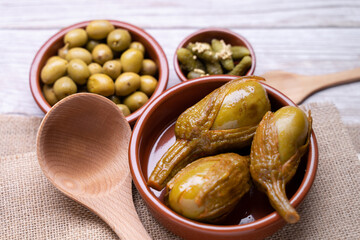 Seasoned olives, pickles in vinegar and Almagro aubergines in a brown bowl on a straw coaster