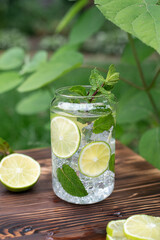 Healthy summer drinks, glass with refreshing lemonade with lemon slices and mint litters on wooden background outdoors.