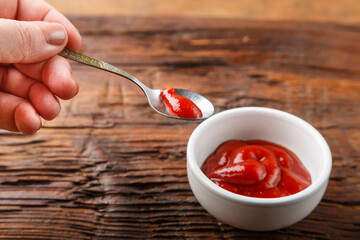 White gravy boat with ketchup and hand with a spoon of sauce on a wooden table.