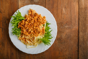 A plate of bolognese pasta decorated with herbs on a wooden table.