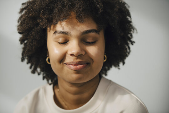 Leende ung kvinna med slutna &ouml;gon framf&ouml;r vit bakgrund