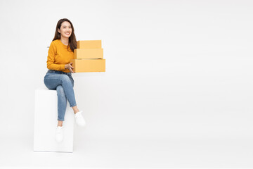 Happy smiling Asian woman holding package parcel box and sitting on white box isolated on white background, Delivery and online shopping express concept, Full Length people composition