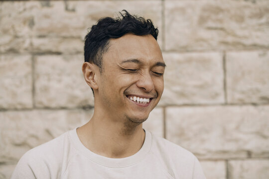 Skrattande man med slutna &ouml;gon st&aring;r framf&ouml;r beige v&auml;gg