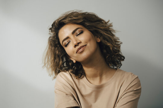 Leende kvinna med slutna &ouml;gon framf&ouml;r vit v&auml;gg