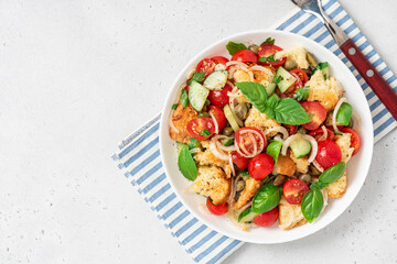 Panzanella - Italian salad from vegetables and bread. Salad with tomatoes, onions, cucumbers, bread, capers and basil in a white plate on a gray concrete background. Vegan salad, Italian cuisine
