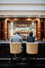 Vertical back view portrait of two successful business people at bar in hotel lobby during business...