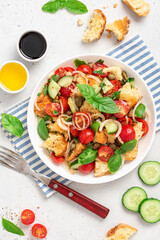 Panzanella - Italian salad from vegetables and bread. Salad with tomatoes, onions, cucumbers, bread, capers and basil in a white plate on a gray concrete background. Vegan salad, Italian cuisine