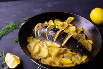 mackerel baked with lemon, potato, rosemary herb in pan on black wooden table