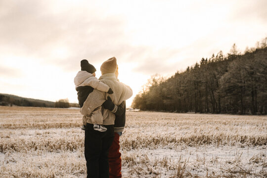Par h&aring;ller dotter i famn st&aring;ende och tittar p&aring; solnedg&aring;ng