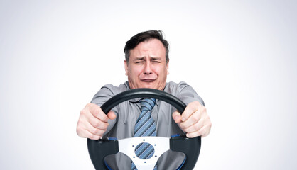 Emotional male businessman in a shirt and tie, closing his eyes and holding a car steering wheel,...