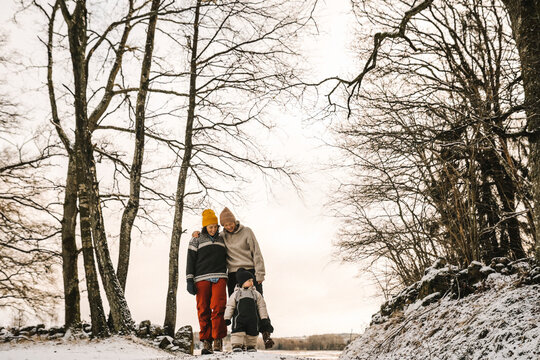 Leende par promenerar med dotter utomhus i sn&ouml;n