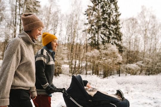 Glatt par promenerar med barnvagn utomhus i sn&ouml;n