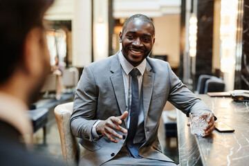 Portrait of smiling African-American businessman talking to partner at bar in hotel during business...