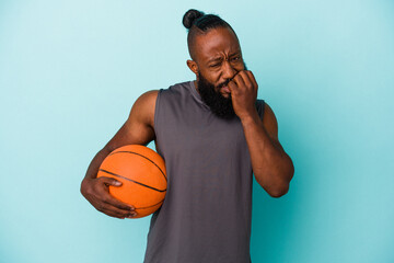 African american man playing basketball isolated on blue background biting fingernails, nervous and...