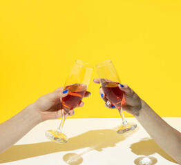 Glasses of drink in hands on yellow and white background. Minimal party arrangement.