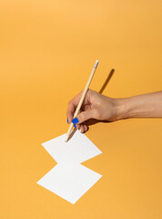 Pencil in woman hand who write notes on orange background.. Minimal business concept.