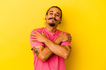 Young caucasian man with long hair isolated on yellow background hugs, smiling carefree and happy.