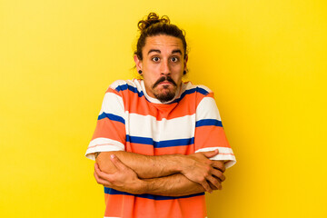 Young caucasian man with long hair isolated on yellow background shrugs shoulders and open eyes...