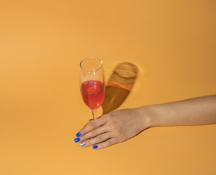Glass of red wine in woman hand on orange background. Minimal party arrangement.