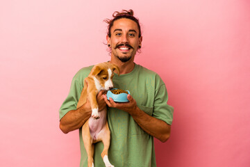 Young caucasian man holding his puppy and his food isolated on pink background