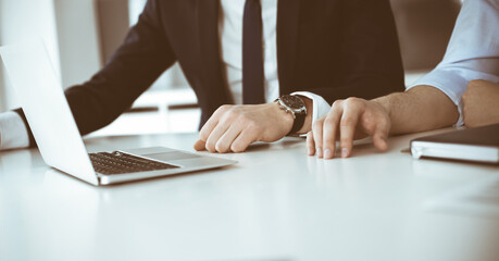 Unknown business people using laptop computer at the desk in modern office. Businessman or male entrepreneur is working with his colleague. Teamwork and partnership concept